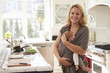 © Monkey Business - Portrait Of Busy Mother With Baby In Sling At Home