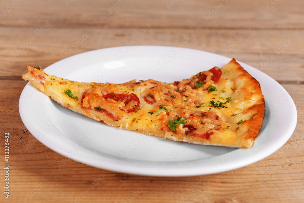 Tasty slice of pizza on plate on wooden table
