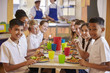 © Monkey Business - Kids at a table in a primary school cafeteria look to camera