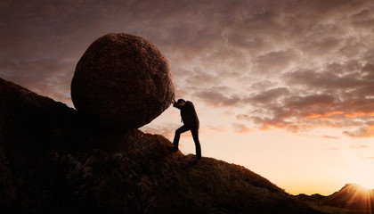 young businessman pushing large stone uphill