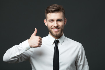 Handsome businessman showing thumbs up sign on dark gray backgro