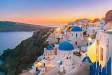 Picturesque View, Old Town Of Oia Or Ia On The Island Santorini, White Houses And Church With Blue Domes At Sunset, Greece
