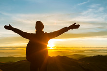 Happy Celebrating Winning Success Woman At Sunset Or Sunrise Standing Elated With Arms Raised Up Above Her Head In Celebration Of Having Reached Mountain Top Summit Goal During Hiking Travel Trek.

