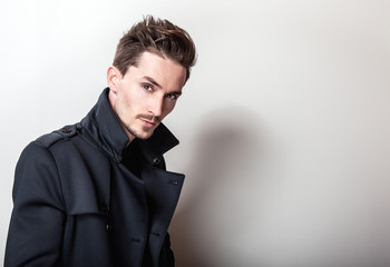 Elegant young handsome man in long stylish dark blue coat. Studio fashion portrait.
