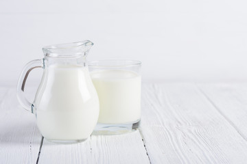 Glass of milk with small jug of milk on white wooden table still life