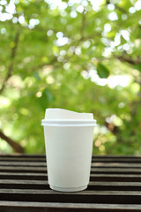 Poster - White paper coffee cup on wooden with green leaves background