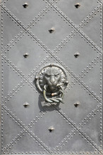 A Fragment Of An Old Metal Door With A Stylized Lion Head Holding A Ring.