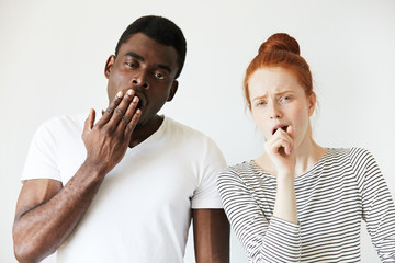 Wall Mural - Mixed-race couple: African man standing next to his redhead Caucasian girlfriend, yawning, covering mouth. looking at the camera with tired and sleepy expression. Human face expressions and emotions