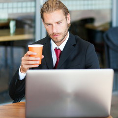     Handsome businessman enjoying a cup of coffee and using his laptop