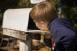 © goodmoments - School boy opening a post box and checking mail. Kid waiting for a letter, checking correspondence and looking into the in the metal mailbox.