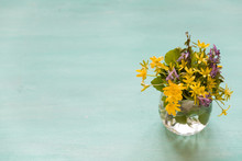 Beautiful Bunch Of Wild Spring Flowers In A Glass Vase On The Turquoise Background. Spring Bouquet Of Yellow And Blues Flowers.