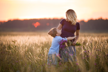 cute kid boy hugging his mother on a summer meadow on beautiful summer sunset. happy family together