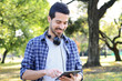 © Mego-studio - Young man using tablet with headphones in park.