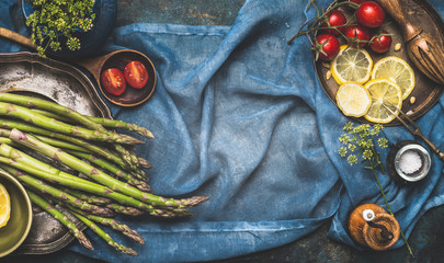 Green asparagus and vegetables cooking ingredients on dark blue rustic background, top view, place for text, banner