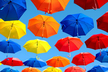 Multicolored Umbrellas Hanging Over Head On The Street Against The Blue Sky And Swinging In The Wind