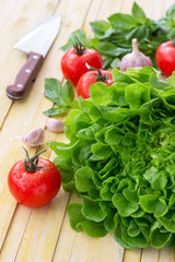 Wall Mural - Fresh lettuce, tomato, basil and garlic for a light summer salad on a wooden surface, selective focus