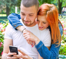 A picture of a joyful couple using smartphones in the park