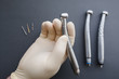 Hand of dentist in latex protective gloves holding dental drill handpiece. Flat lay of dental handpiece in dentist hand on gray background. Dental handpieces and bur tools on background
