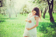 Pregnant woman in the apple orchard is holding tummy