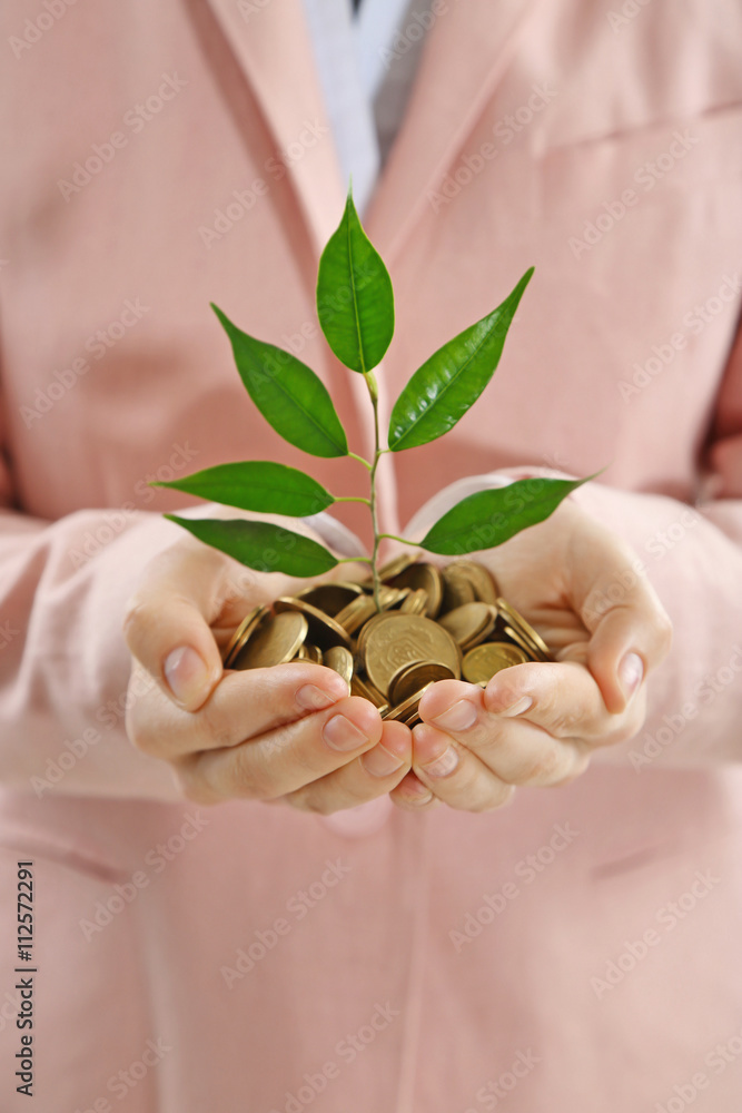 Hands holding plant sprouting from a handful of coins on white background
