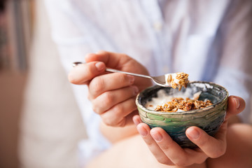 Young woman with muesli bowl. Girl eating breakfast cereals with nuts, pumpkin seeds, oats and yogurt in bowl. Girl holding homemade granola. Healthy snack or breakfst in the morning..