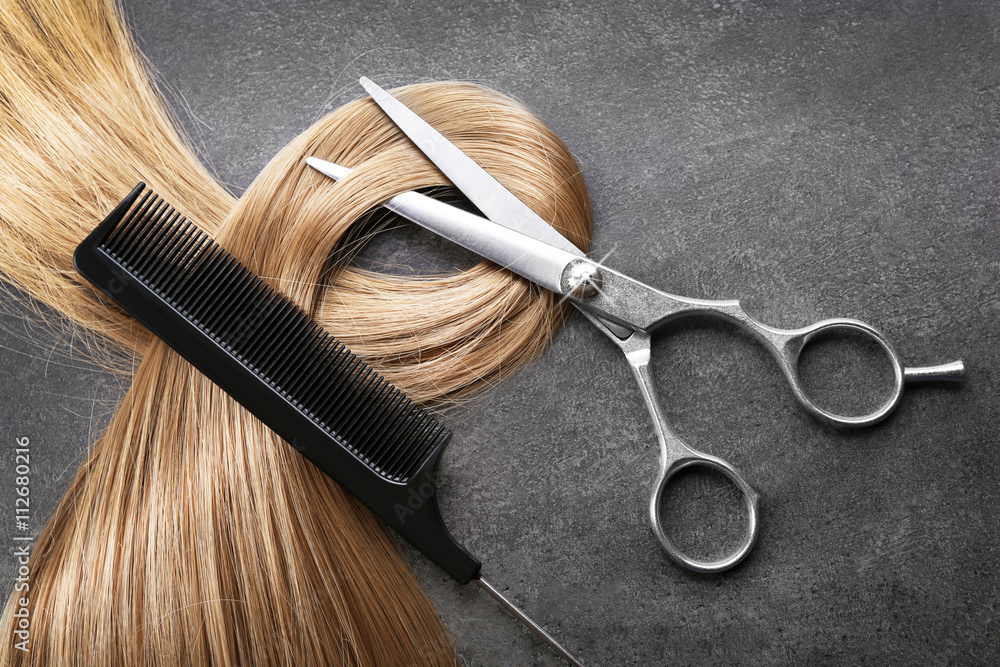 Hairdresser's scissors with comb and strand of blonde hair on grey background - obrazy, fototapety, plakaty 