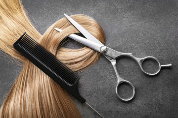 hairdresser's scissors with comb and strand of blonde hair on grey background