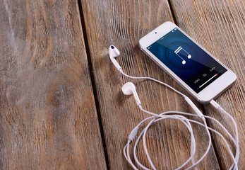 Sticker - White smart phone with headphones on wooden background