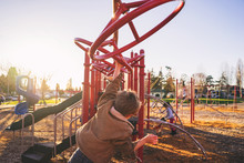 Rear View Of Boy Swinging On Monkey Bars In Playground