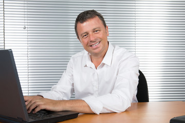 Poster - Attractive office worker sitting at desk smiling at camera