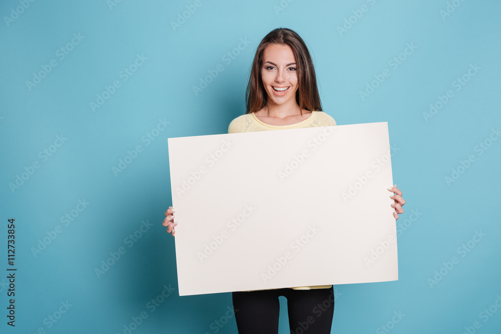 Pretty young woman holding empty blank board over blue background - obrazy, fototapety, plakaty 