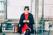 © Eugenio Marongiu - Young beautiful red dressed vintage hipster woman sitting at bus stop using smart phone hand hold tapping touchscreen - technology, commuter, social network concept