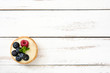 Delicious tartlet with raspberries and blueberries on a white wooden table
