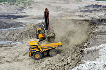 Wall Mural - Yellow excavator loading soil on a truck at mine back lit