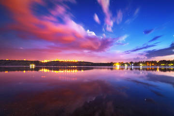 Wall Mural - Colorful night landscape on the lake with blue sky and moving clouds reflected in water. Nature background