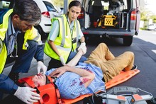 Emergency Medical Technicians Healing Injured Man On Road