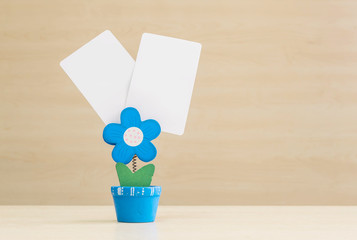 Wall Mural - Closeup clamp photo in blue flower shape shape in flowerpot with black white paper on blurred wooden desk and wall background