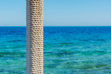 Wooden Pole With Rope Entwined On A Background Of Blue Sea And Sky