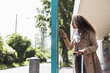 © Westend61 - Young woman with luggage and cell phone at bus stop