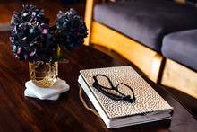 Book, Reading Glasses And Flower Arrangement On Coffee Table