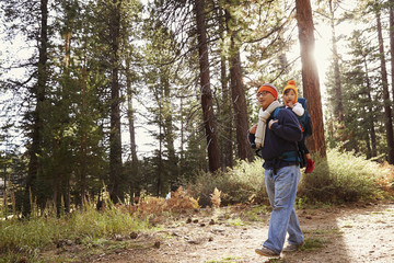 Wall Mural - Dad walking in forest with toddler daughter in baby carrier