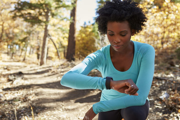 Wall Mural - Young black woman kneeling in a forest checking smartwatch