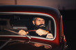 © endrews21 - brutal bearded man with a smart mustache brunette sitting in a dark saloon car retro evening at sunset
