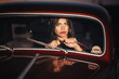 © endrews21 - beautiful brunette girl with big brightly painted red lipstick lips and in a short dress on high heels next to a retro car on a rural road at sunset