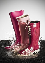 Three Pink Rubber Boots Splashing In A Puddle