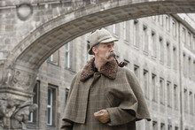 A Man Dressed Up As Sherlock Holmes Standing Under A Building Arch Looking Away