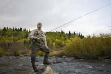 A Man Standing On A Rock While Fly Fishing In A River