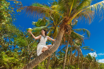 Young beautiful bride with coconut on the palm tree on a tropica