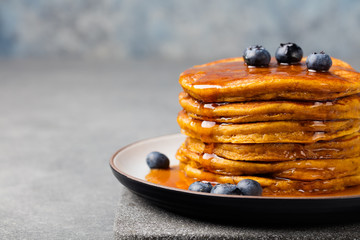 Wall Mural - Pumpkin pancakes with maple syrup and blueberries on a plate. Grey stone background