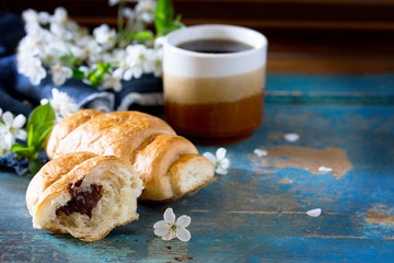 Mug of coffee and a croissant on the vintage wooden table, space